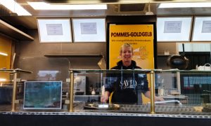 Mitarbeiterin im Foodtruck „Pommes Goldgelb“ in Verden lächelt hinter der Theke der evangelischen Pommesbude.